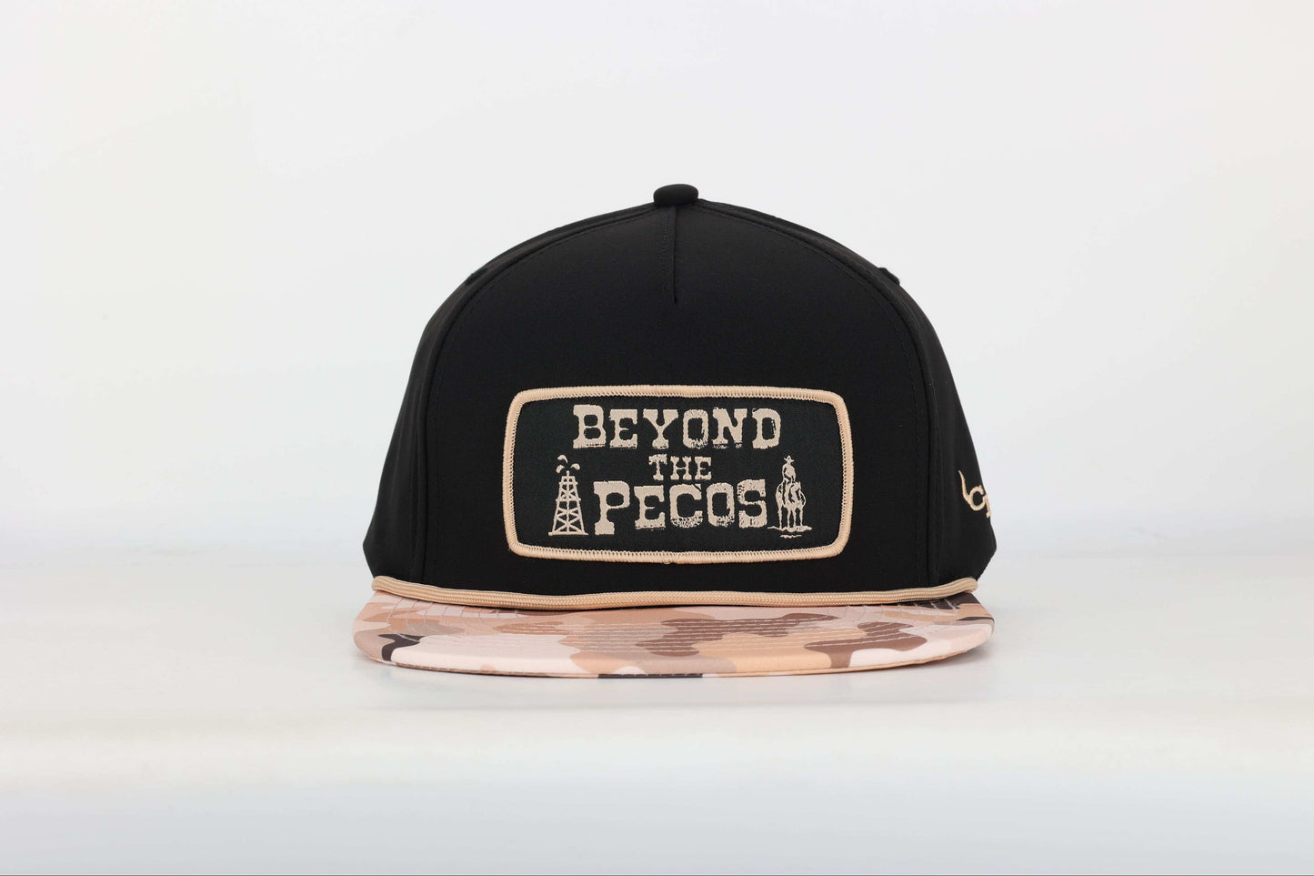 Black snapback cap with "Beyond the Pecos" woven patch on the front in old gold, featuring an oil rig and cowboy graphic, old gold rope, and a desert camo print bill. Front View
