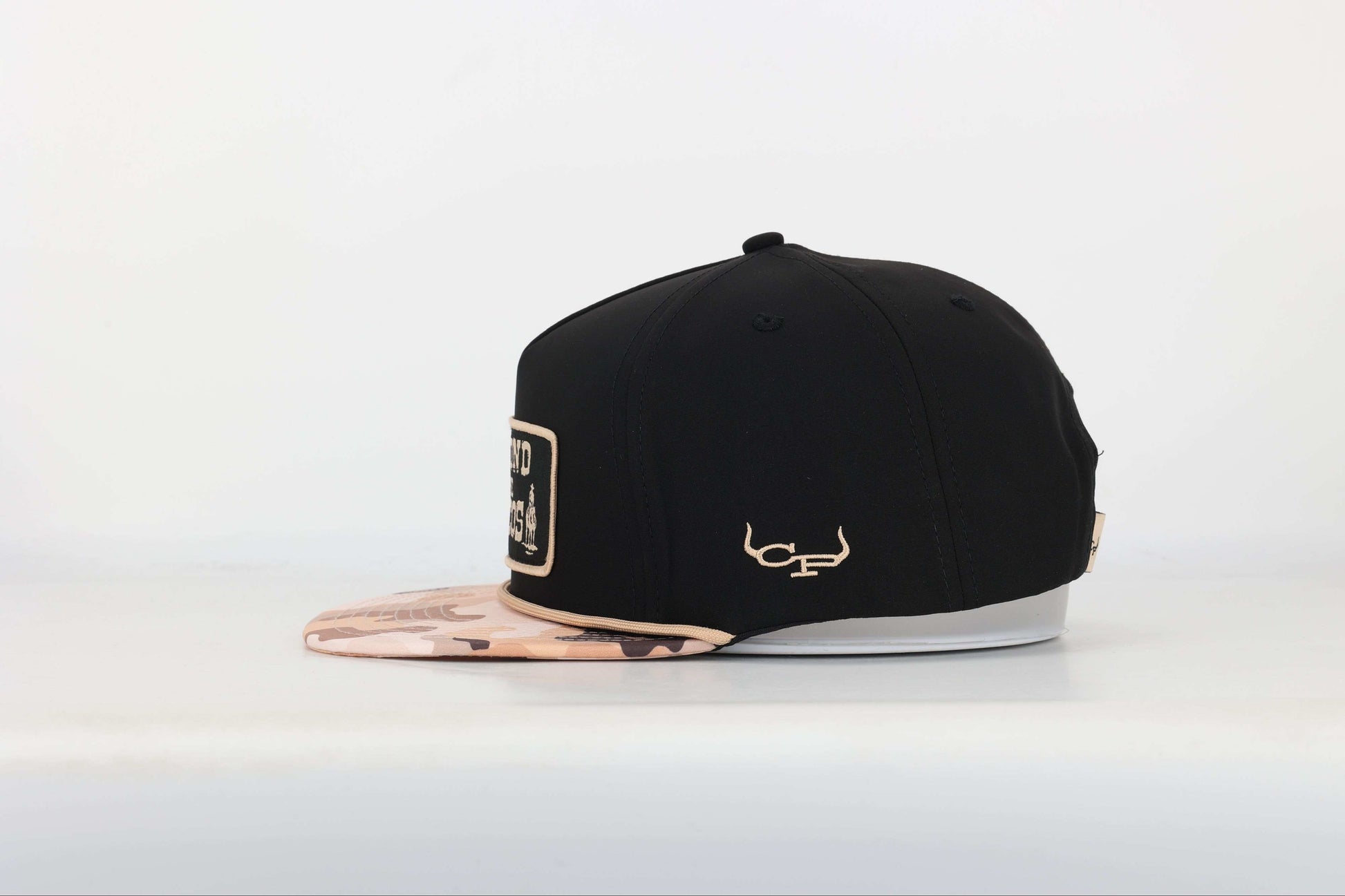 Black snapback cap with "Beyond the Pecos" woven patch on the front in old gold, featuring an oil rig and cowboy graphic, old gold rope, and a desert camo print bill. Right Side View
