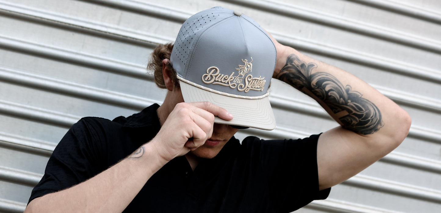 Gavan Hauck wearing a Cowpuncher Thread Company snapback cap with a gold embroidered brand logo that says "Buck the System" against a metallic background.