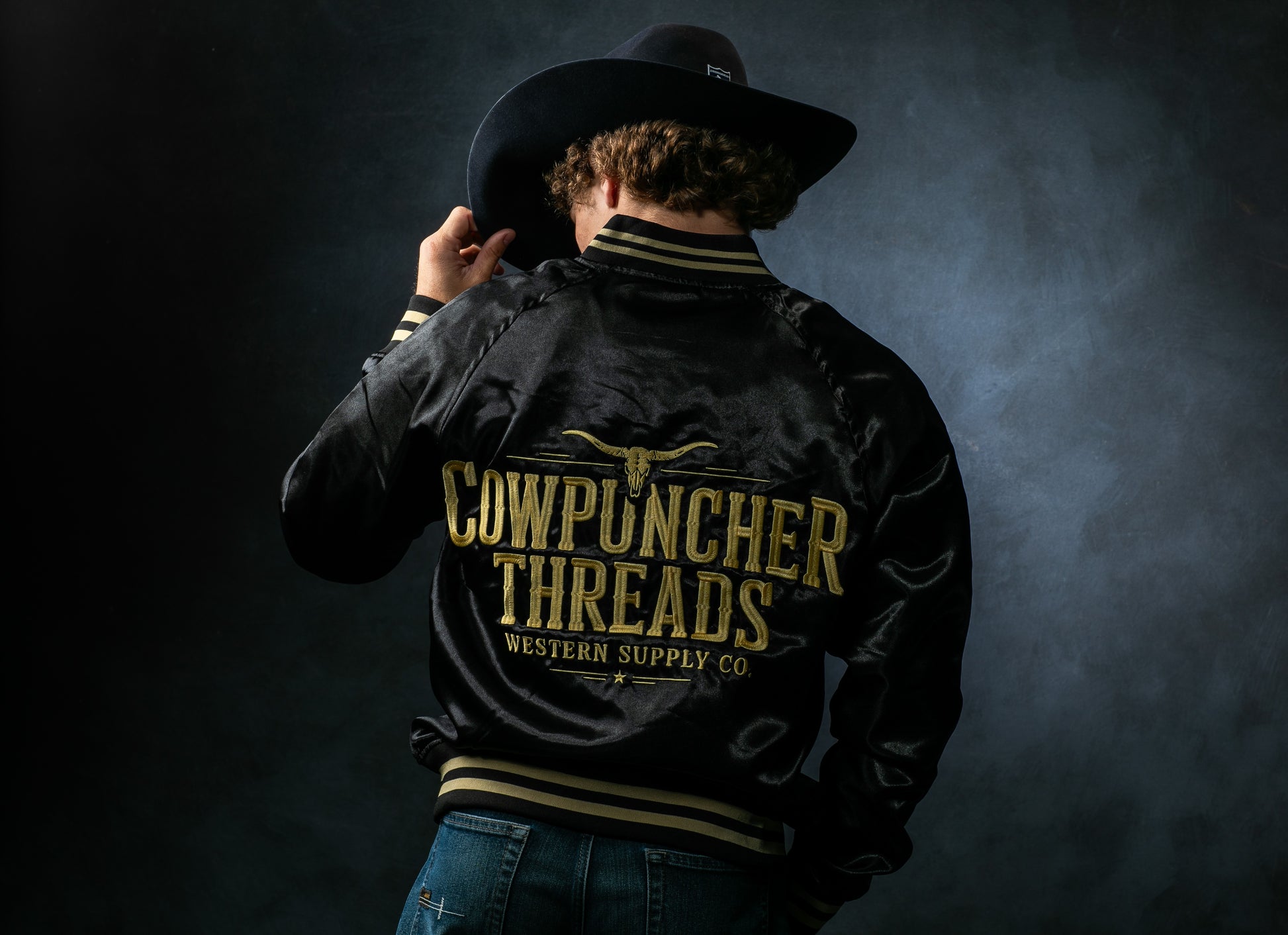 Gavan Hauck, wearing a black satin bomber jacket with a 'Cowpuncher Threads" Logo in gold embroidery on the back.