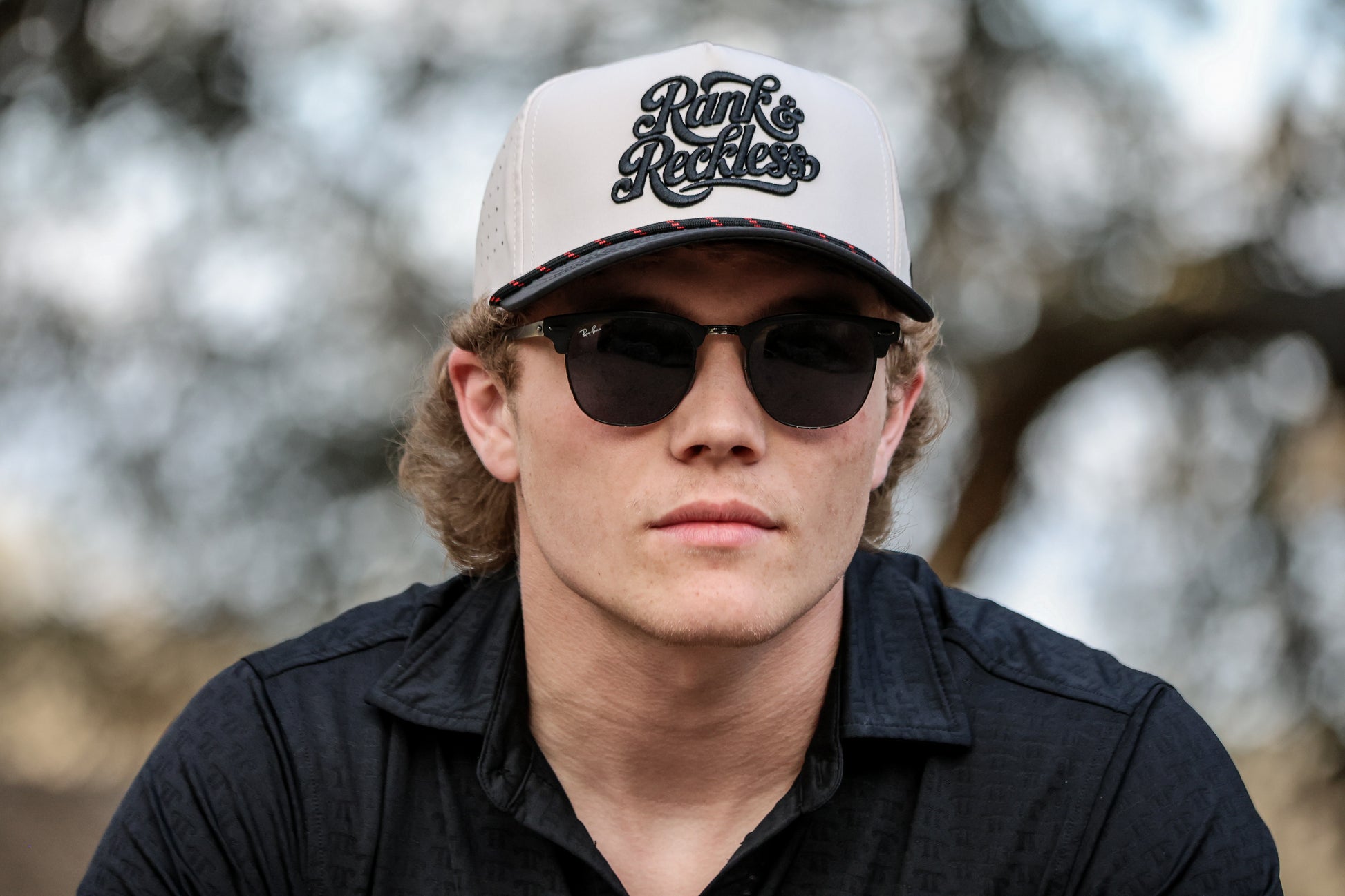 Gavan Hauck wearing a snapnback cap with 'Rank & Reckless' logo and sunglasses outdoors