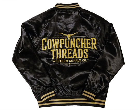 Black satin rodeo bomber jacket with 'Cowpuncher Threads' logo in gold embroidery on a transparent background.